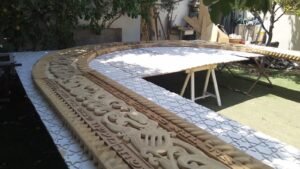 קשת עץ מגולפת עם כתובת עברית מורכבת על לוחות סבכה לבנים בחצר