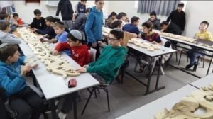 ילדים בכיתה מלטשים חלקי עיטור מגולפים מעץ המונחים על השולחנות