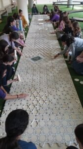 יריעת הסבכה הארוכה נפרשת לכל אורך המתחם, מוקפת בנות העוסקות בהרכבתה