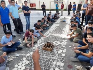 תלמידים בחצר בית הספר מרכיבים סבכת כוכבים לבנה, ובמרכזה דגם עץ של המקדש