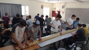 תלמידי ישיבה בכיתה מלטשים פס גילוף ארוך הפרוש על שולחנות