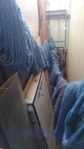 אגודות צמר צבועות בגוני תכלת וכחול תלויות לייבוש בסדנה