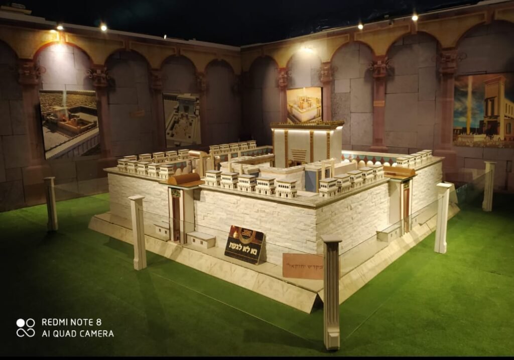 דגם בית המקדש במרכז אולם תצוגה המעוצב כחצר עתיקה עם קשתות ותמונות