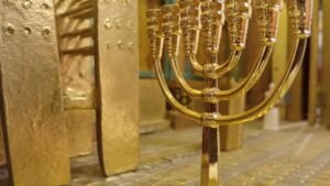 מנורת זהב זעירה בת שבעה קנים בתוך היכל הדגם, על רקע קירות ודלתות מצופים זהב