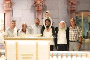 צוות הבונים וילד מצטלמים מאחורי חומת דגם בית המקדש השלישי במיני ישראל
